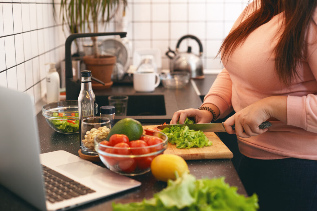 female standing at kitchen counter and cutting fresh organic vegetables on chopping board, making healthy low calories salad