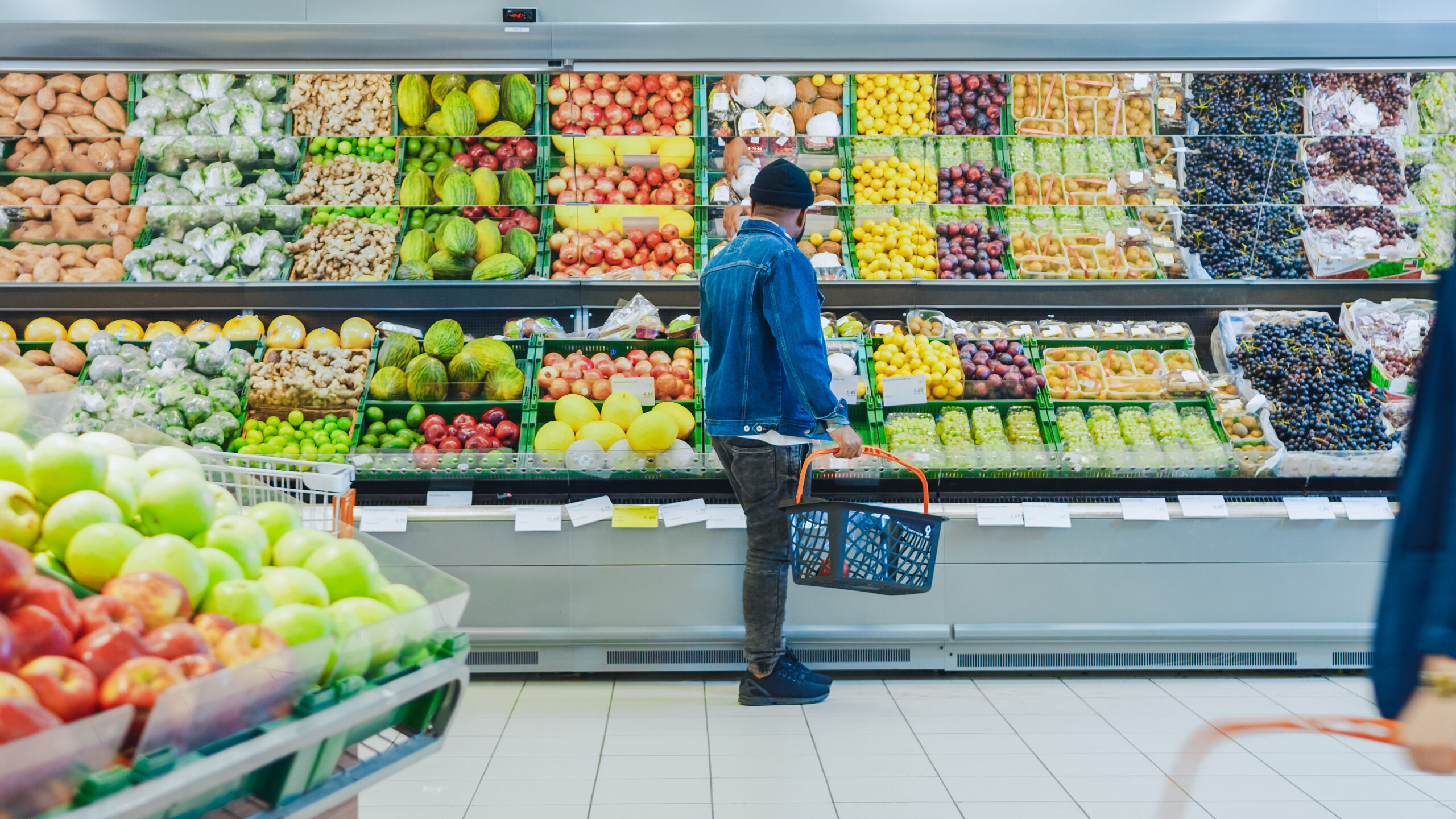 Man stands in fresh and organic fruits and vegetable isle in the produce section of the store contemplating inflation prices as he selects food