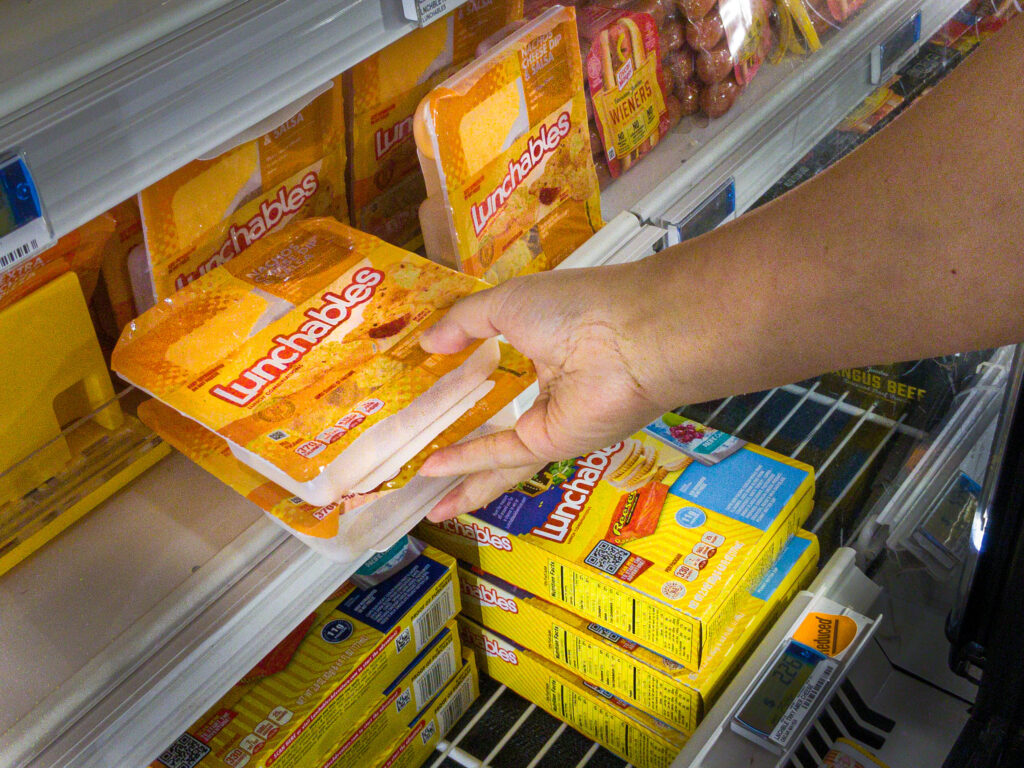 Shiloh, IL--July 10, 2021; hand of shopper reaching into refrigerator section of grocery store selecting two Oscar Meyer Lunchable packages, a Kraft-Heinz brand of food. 
By Philip